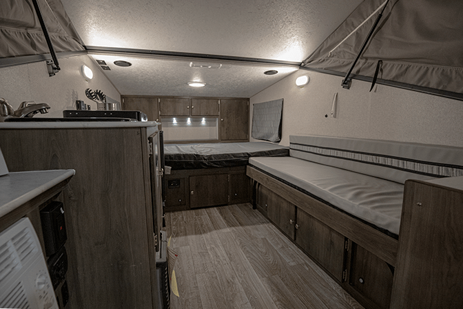 A view from the rear entrance of the Coachmen Clipper 12.0TD XL pop up camper RV shows the kitchenette on the left, the gaucho on the right and the main bed at the front of the trailer.