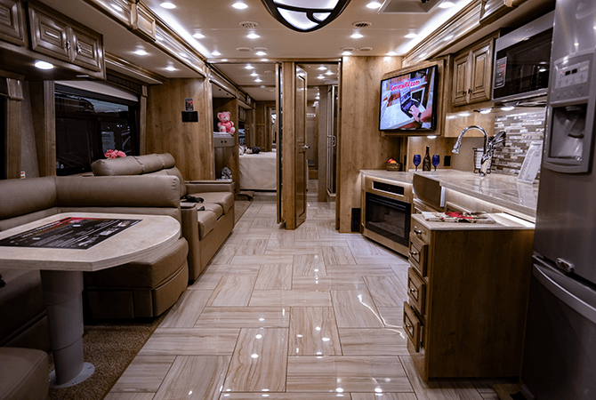 A view from front to back inside the Discovery LXE 40G motorhome by Fleetwood RV. This RV floor plan features a wide open living and dining area. Midway back into the RV, a set of folding doors reveals a bunkroom on the passenger side and a bathroom on the driver's side of the coach. 