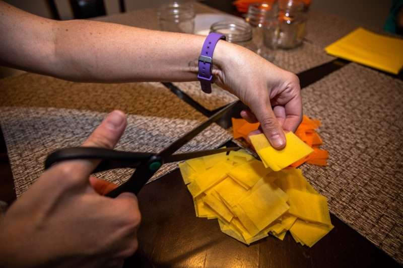 A woman cuts up yellow and orange tissue paper using scissors.