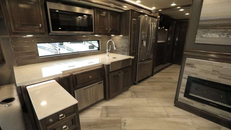 A photo of the kitchen and dining area inside the Fleetwood Di Discovery LXE 40M. This luxurious motorhome a residential size fridge with French doors, a pull-out island for additional counter space, a dishwasher, convection microwave oven, fireplace, and many other high end touches. 