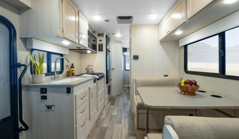 An interior view from the front of the Winnebago Outlook looking towards the back of the RV. The galley kitchen is on the passenger side and across from a dinette booth. 