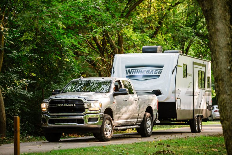 A truck pulling the Winnebago Micro Minnie 2100BH on a road surrounded by trees.